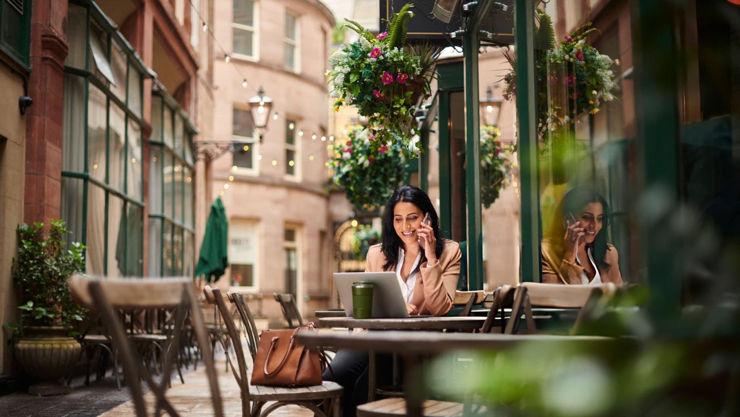 A woman checking her finances on her phone at a leafy outdoor cafe