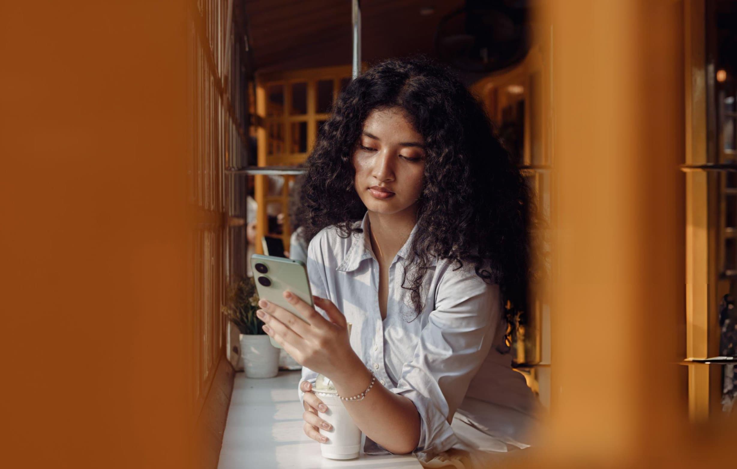 A woman checking her finances on her phone in a warm cafe